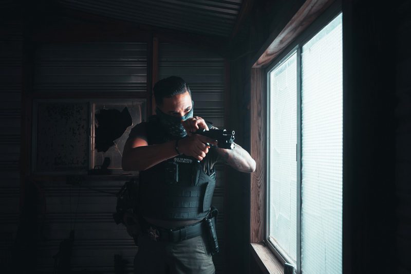 A soldier in a bulletproof vest by the window checks his weapon