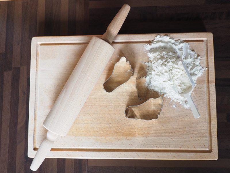 A wooden board with a pile of flour, foot molds and a rolling pin on it