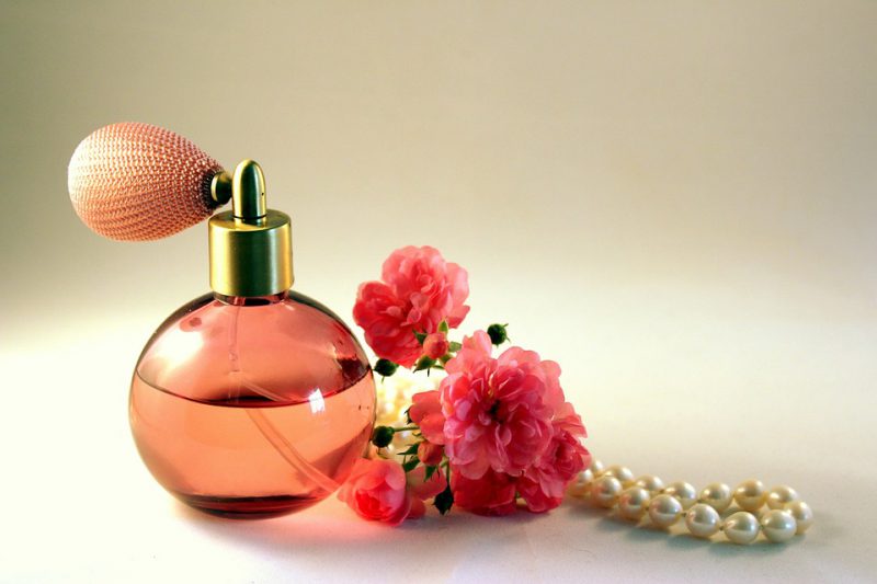 Perfume with flower and necklace next to it