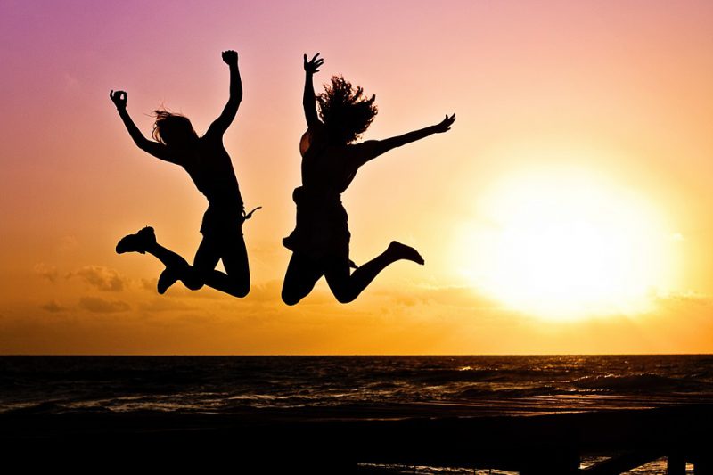Two girls on the beach are jumping at sunset