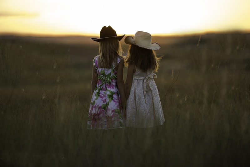 Sisters hold each other and stand in the pasture in the sunset