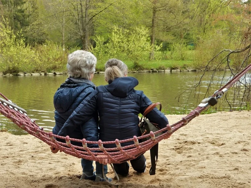 Two women are sitting in a hammock on the river bank