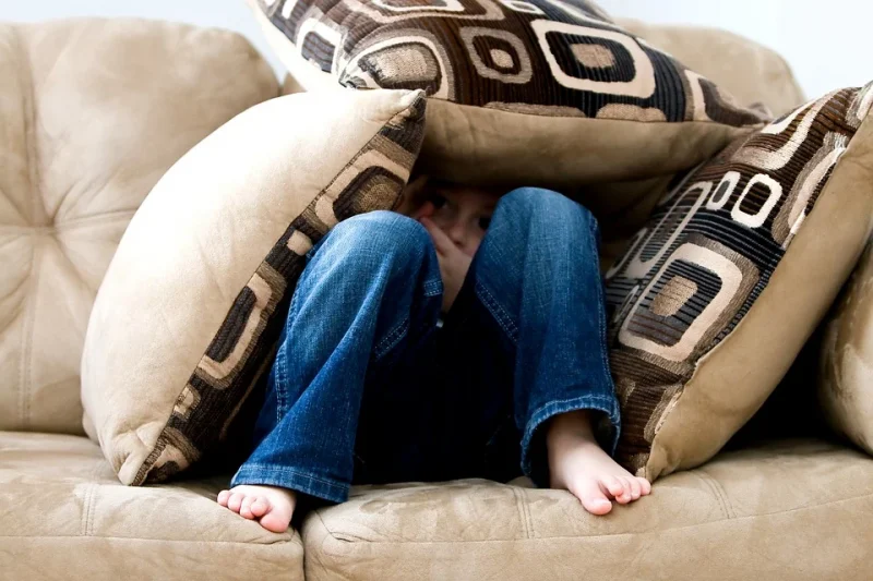 A toddler is sitting on the bed covered with pillows