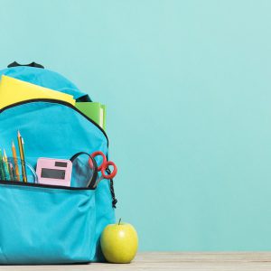 School backpack with accessories and a green apple next to it