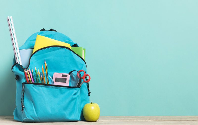 School backpack with accessories and a green apple next to it