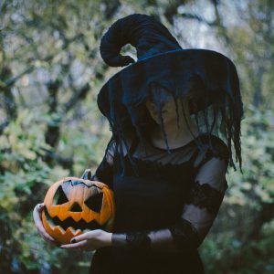 A witch in the forest holds a carved pumpkin