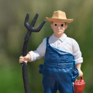 A figure of a farmer with a pitchfork and a red bucket in his hands