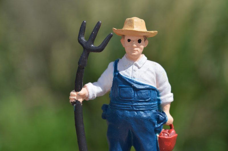 A figure of a farmer with a pitchfork and a red bucket in his hands