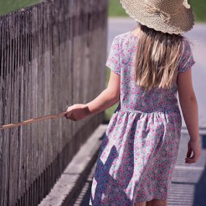 A little girl walks with a cane leaning against the fence
