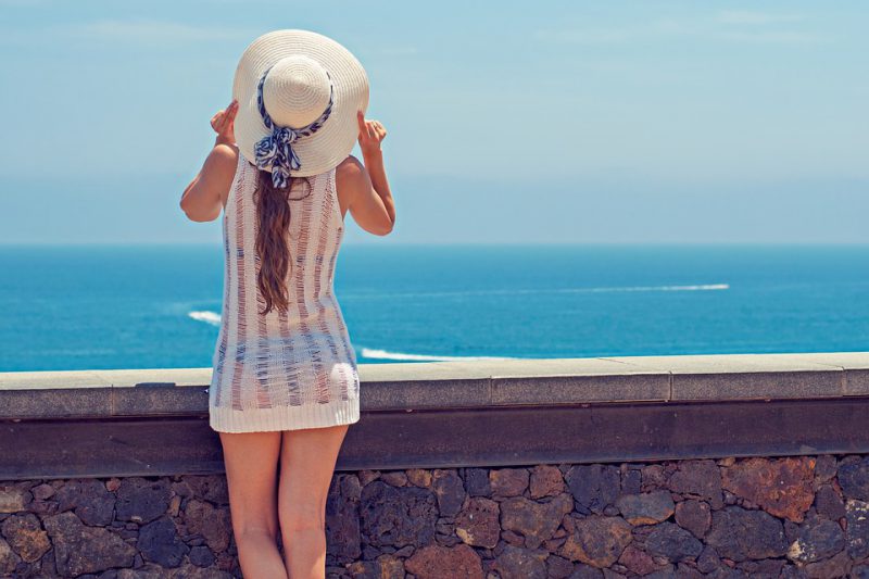 A woman with a hat is looking at the sea